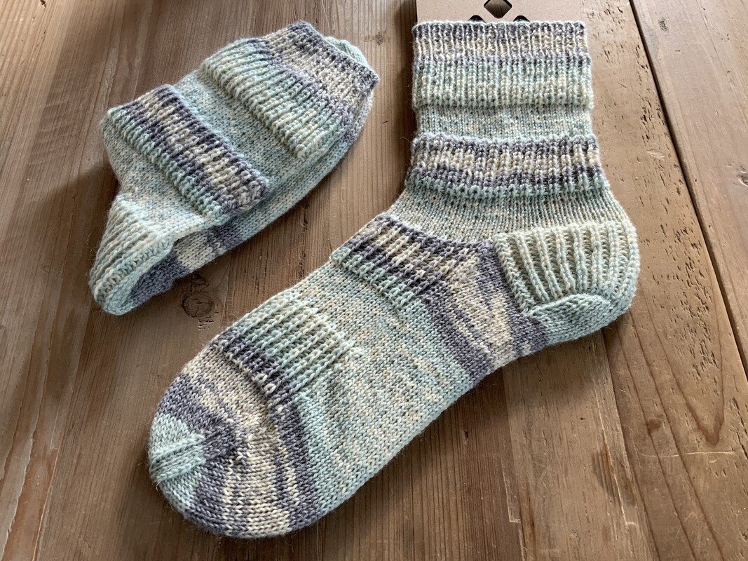 Nahaufnahme zweier handgestrickter Kurzsocken mit geformter Ferse und Rippenbündchen auf Holz