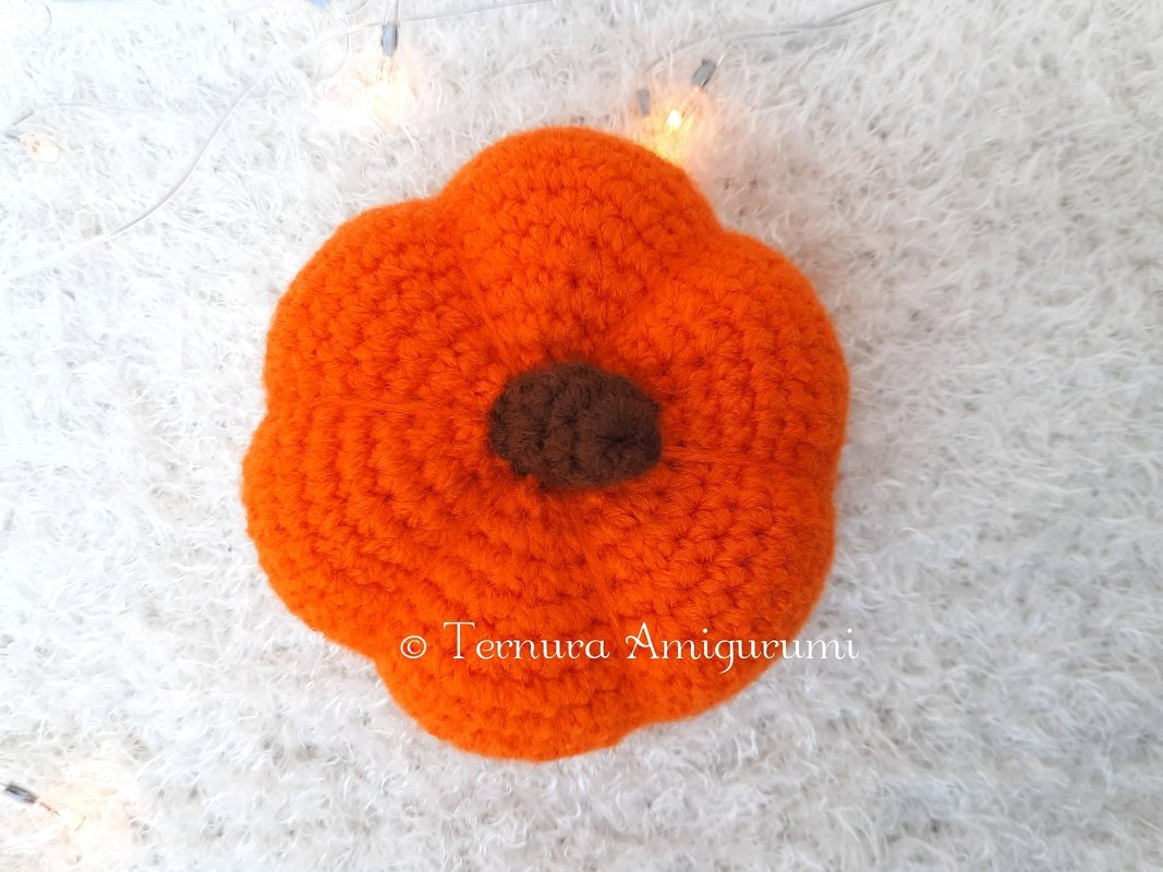 Orange crocheted pumpkin with brown center on white textured background