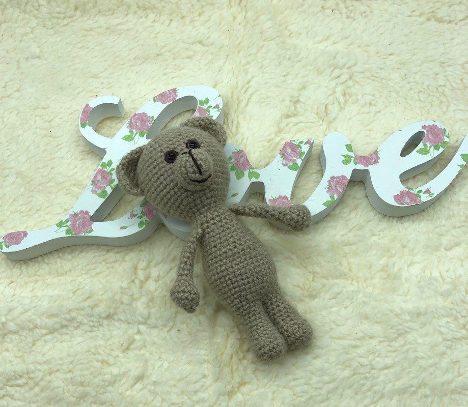 mini Amigurumi Teddybär mit einfachen Proportionen auf flauschiger Oberfläche