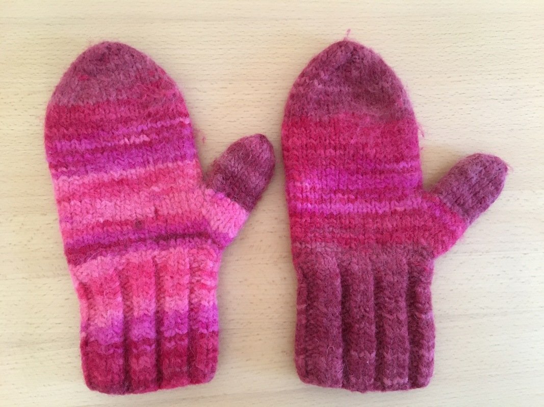 Gestrickte Fäustlinge in Pink- und Magentatönen mit gerippten Bündchen auf hellem Untergrund