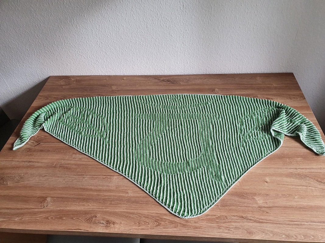Gestricktes Dreieckstuch mit Ripple-Muster und Streifen in Grün und Weiß, auf einem Holztisch liegend.