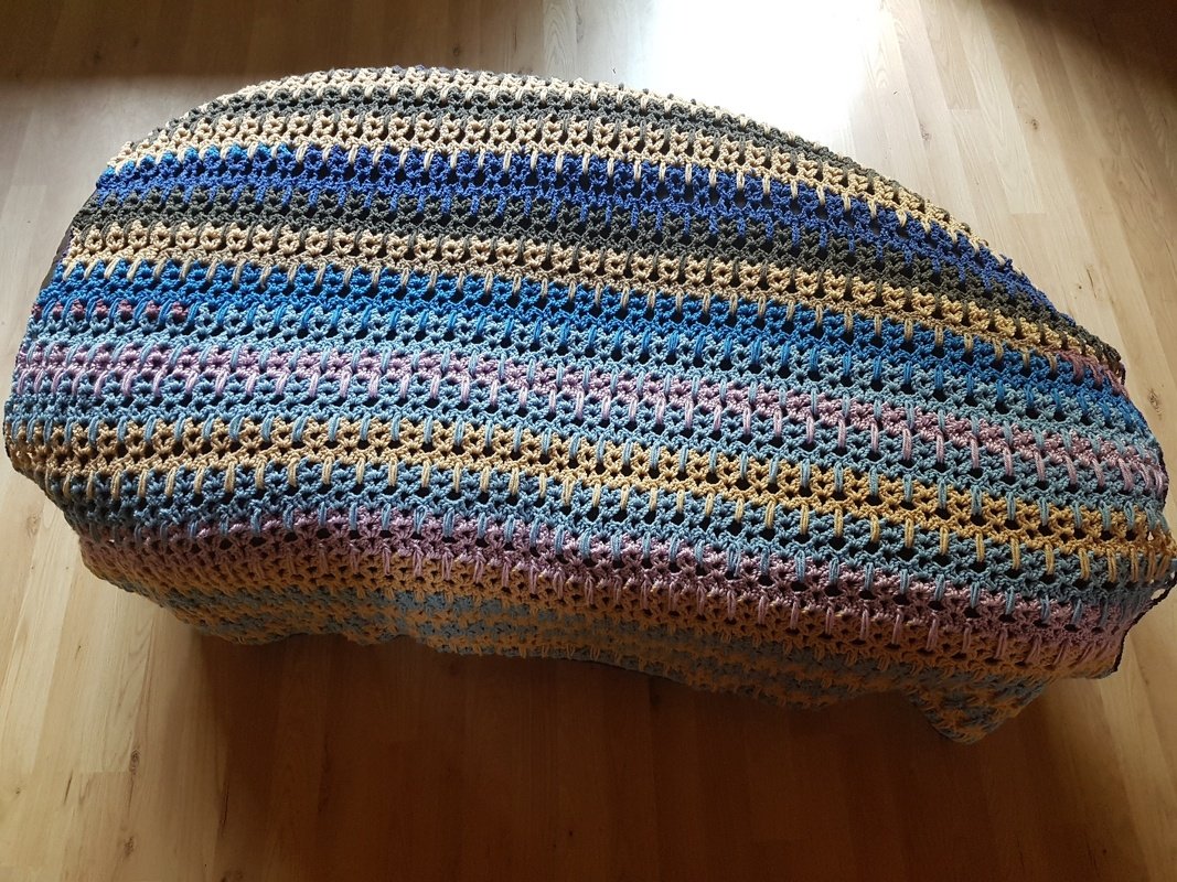 Gehäkelte Decke mit blauen, beigen und pastellfarbenen Streifen auf Holzboden drapiert