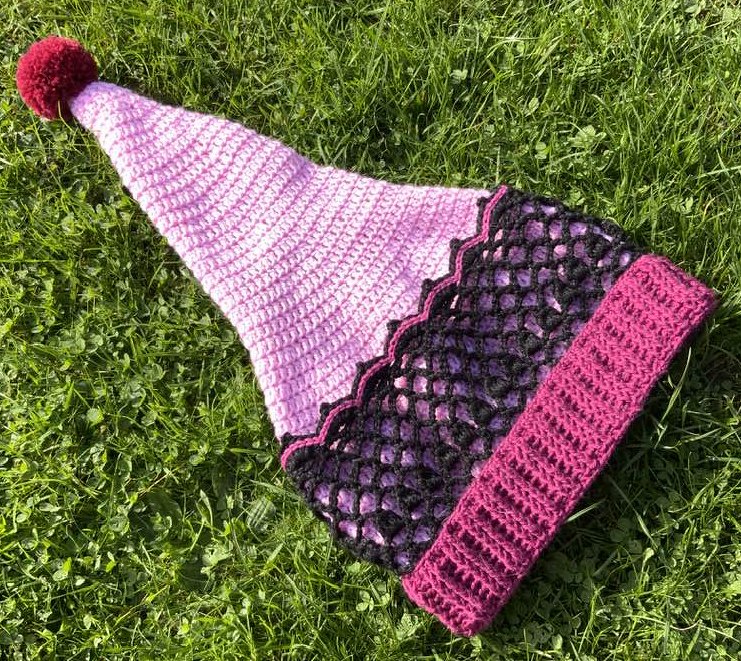 Gehäkelte Zipfelmütze mit Bommel in Rosa, Schwarz und Pink auf Gras