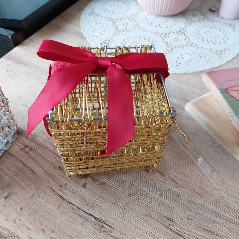 Kleine goldene Drahtbox mit roter Schleife auf Holzoberfläche