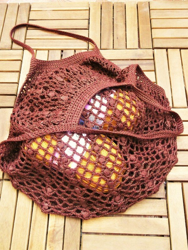 Brown crocheted mesh market bag holding two round yellow objects on a wooden slatted surface.
