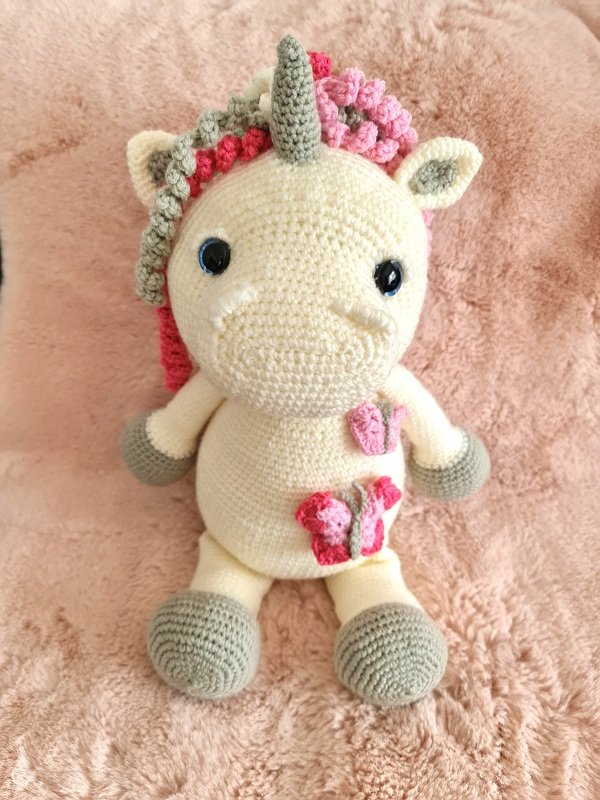 Gehäkeltes Amigurumi-Einhorn creme mit rosa-grauer Mähne und Schmetterling