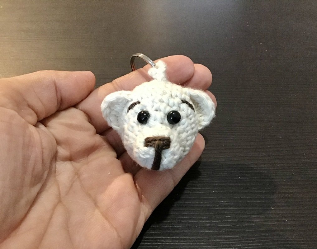 Gehäkelter weißer Teddybärkopf-Schlüsselanhänger in einer Hand