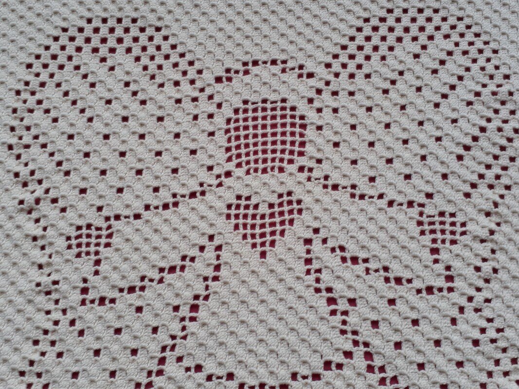 Nahaufnahme des Filet-Häkelmusters einer cremefarbenen Babydecke mit Engel- und Herzmotiv