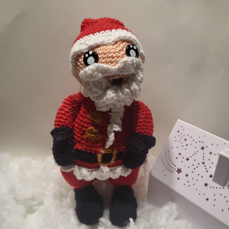 Niedlicher gehäkelter Weihnachtsmann mit krausem weißem Bart, rotem Mantel und schwarzen Handschuhen