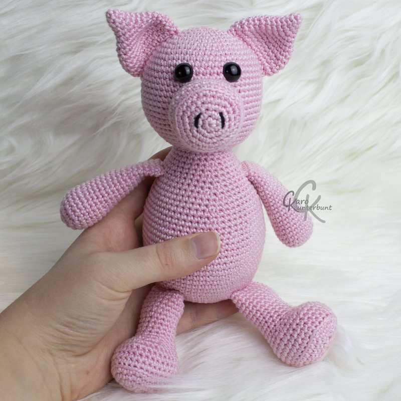 Rosa gehäkeltes Amigurumi-Schwein mit großen Ohren und schwarzen Sicherheitsaugen, in einer Hand gehalten