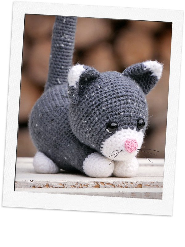 Gehäkelte graue Amigurumi-Katze mit weißen Pfoten und rosa Nase