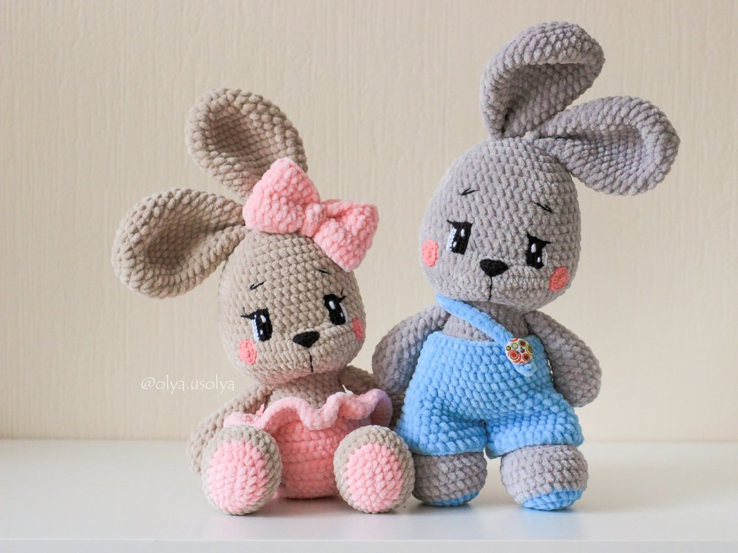 Two amigurumi crochet bunnies: left beige with pink bow and ruffled skirt; right gray in blue overalls with a button.