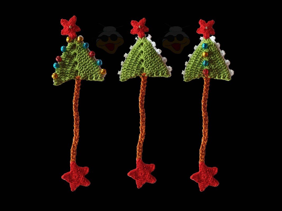 Drei gehäkelte Weihnachtsbaum-Lesezeichen mit roten Sternen, orangefarbener Kordel und bunten Glöckchen auf schwarzem Hintergrund.