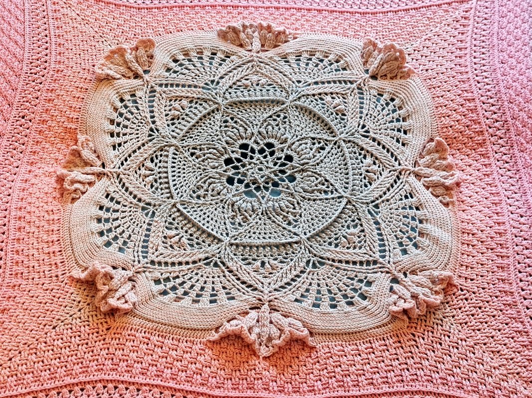 Nahaufnahme einer quadratischen Häkeldecke mit cremefarbenem Mandala auf pastellrosa Grund