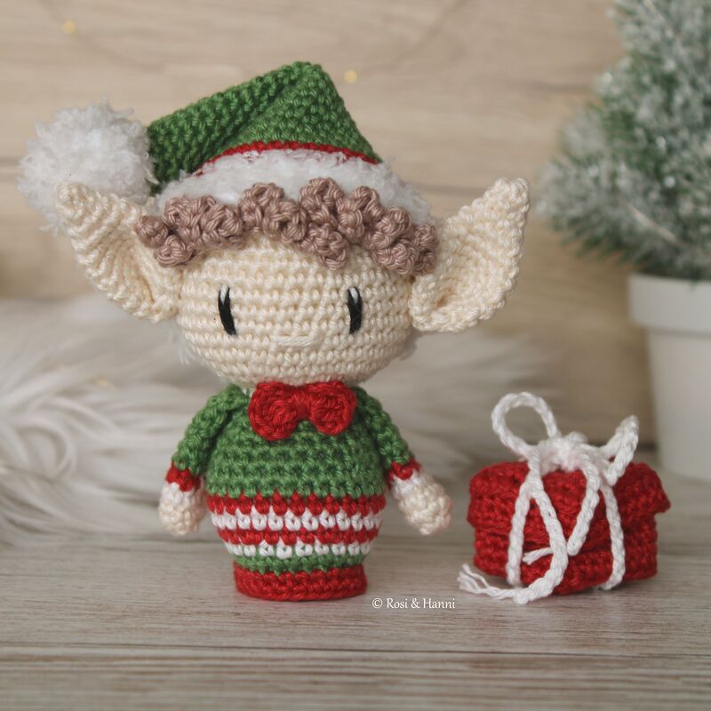Gehäkelter Amigurumi-Wichtel in Grün, Rot und Creme mit Mütze und kleinem Geschenk