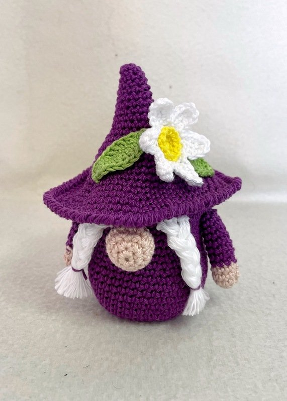 Gehäkelter lila Wichtel mit spitzem Hut, weißer Blüte und geflochtenen Zöpfen