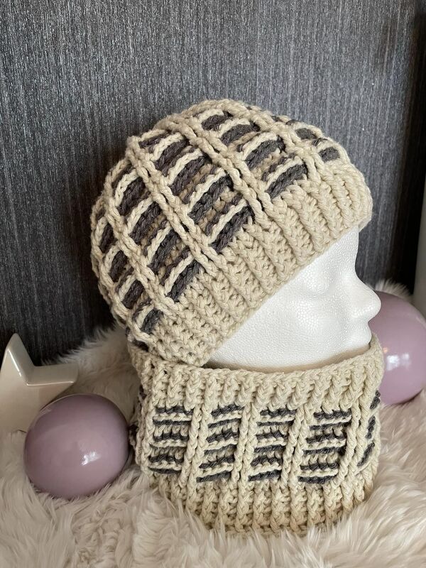 Gehäkelte cremefarbene Mütze und passender Schlauchschal mit grauen Einsätzen auf einer Schaufensterkopf-Büste