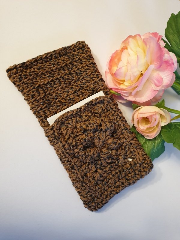 Brown crocheted pouch with flap pocket, a white card visible, and artificial flowers beside it.