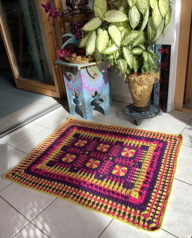Bunter gehäkelter Teppich mit geometrischem Blumenmuster neben Pflanze