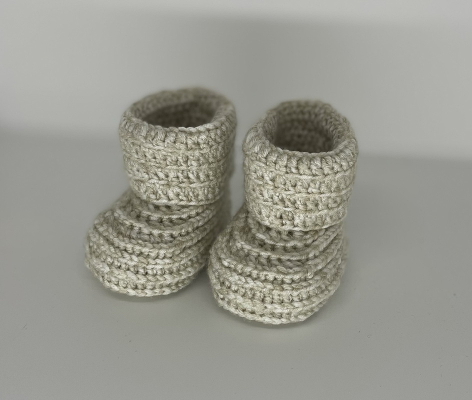 Nahaufnahme von zwei cremefarbenen gehäkelten Baby-Booties mit geripptem Muster und Umschlagbund.