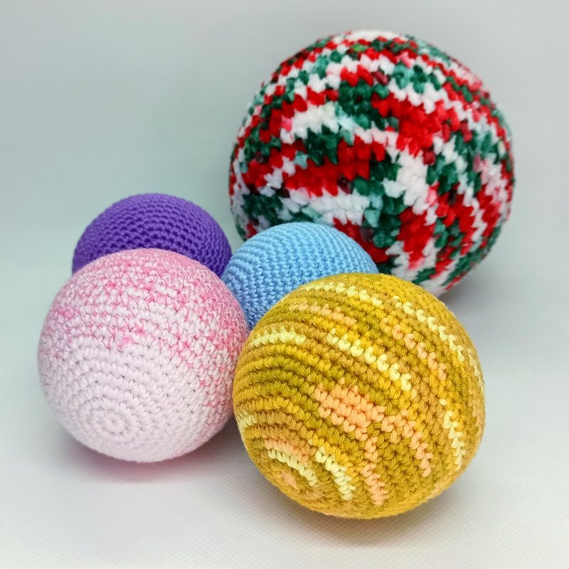 Five crocheted decorative balls in red-green variegated, gold, pink, blue and purple on a pale background