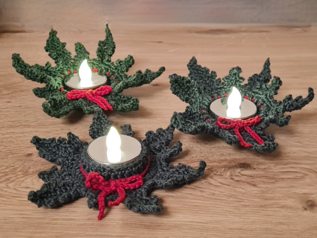 Drei gehäkelte Teelichthalter in Blattform mit roten Schleifen und LED-Teelichtern auf einem Holztisch.