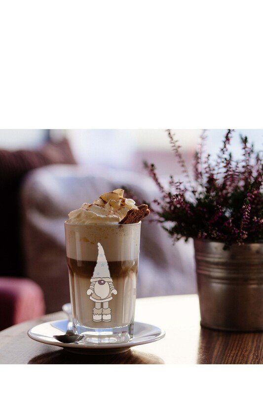 Hoher Latte mit Sahne und Keks, auf dem Glas ein Gnom-Motiv