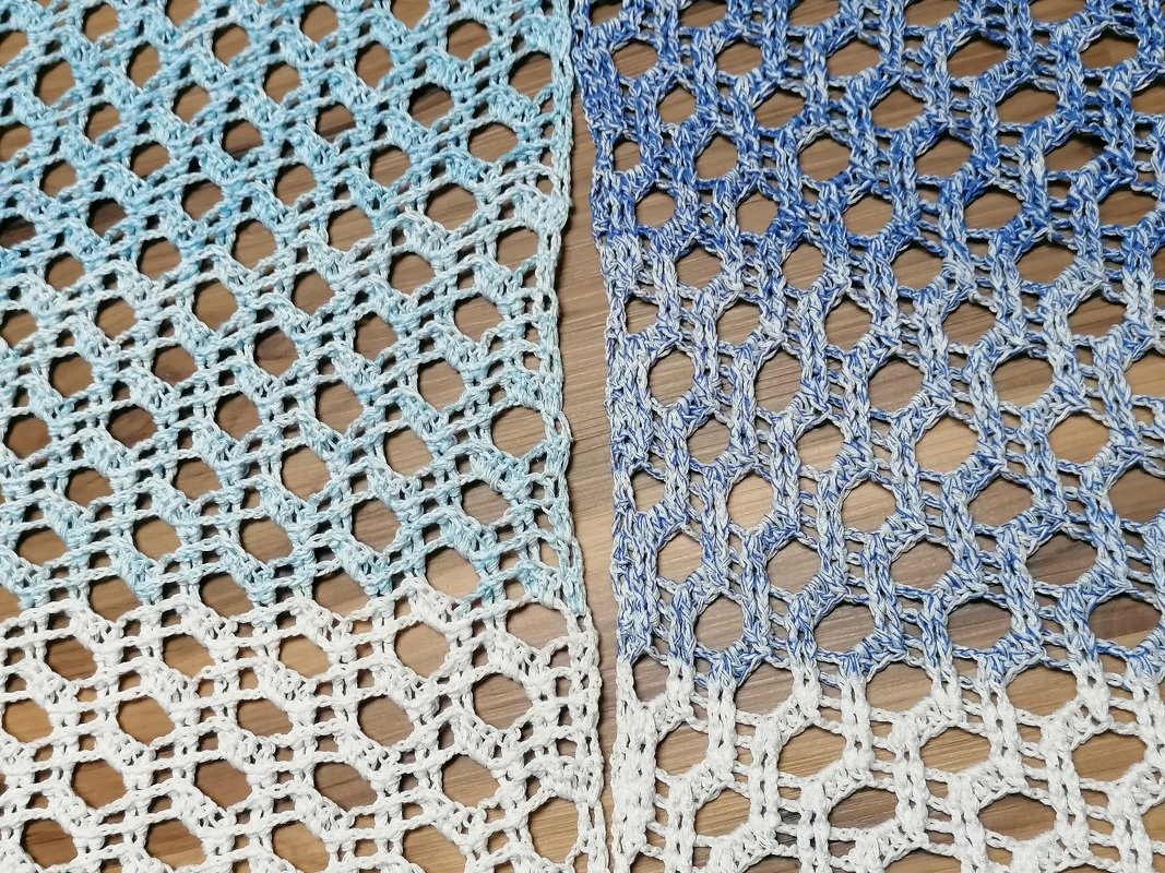 Zwei gehäkelte Proben mit blau-weißem Farbverlauf und offenem Lochmuster auf Holzuntergrund.