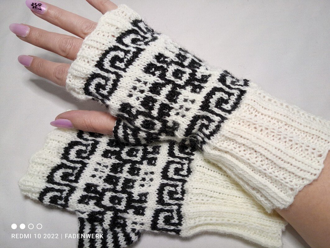 Weiße gestrickte fingerlose Armstulpen mit schwarzem geometrischem Muster an Händen