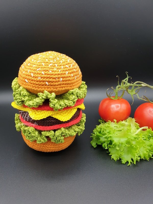 Crocheted burger toy with yarn bun, lettuce, cheese, tomato, and patty
