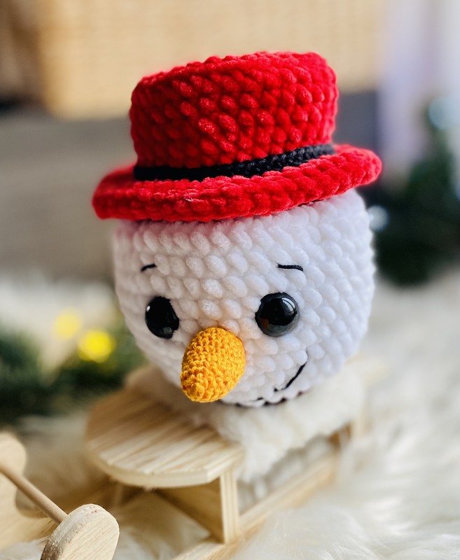Gehäkelter Schneemannkopf mit rotem Zylinder auf Holzschlitten