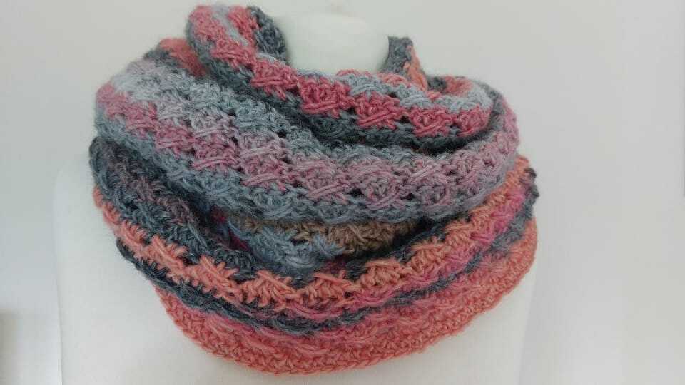 Gehäkelter Loop‑Schal in Grau, Rosa und Pfirsich mit Strukturmuster auf weißer Schaufensterpuppe