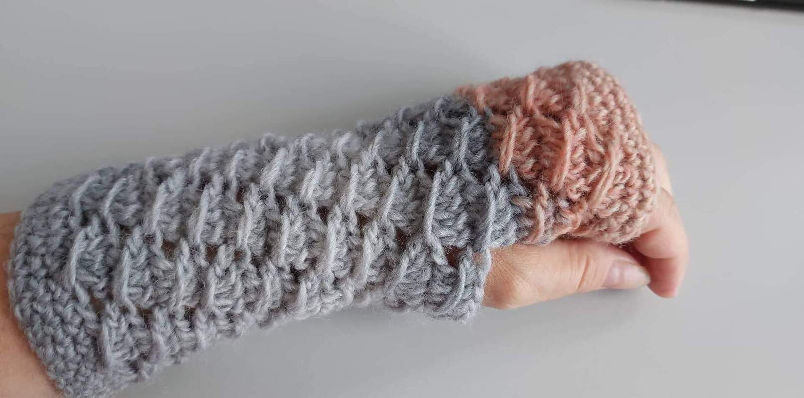 Hand mit gehäkelter, fingerloser Armstulpe grau und rosé Bündchen
