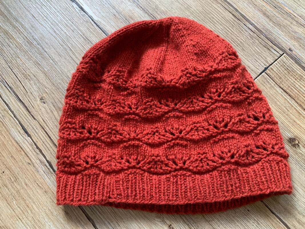 Rote Strickmütze mit Rippenbund und wiederholtem Ajourmuster