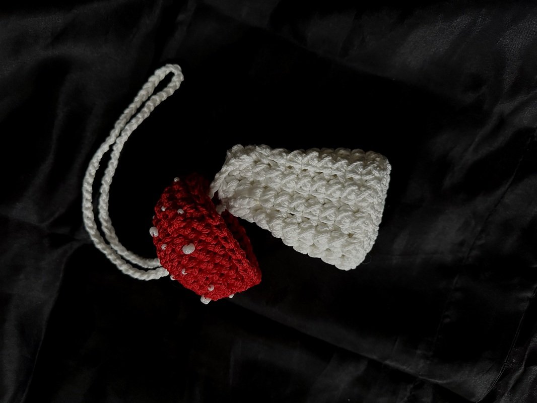 Two small crocheted drawstring pouches on black fabric
— one white textured pouch and one red beaded pouch with a braided cord