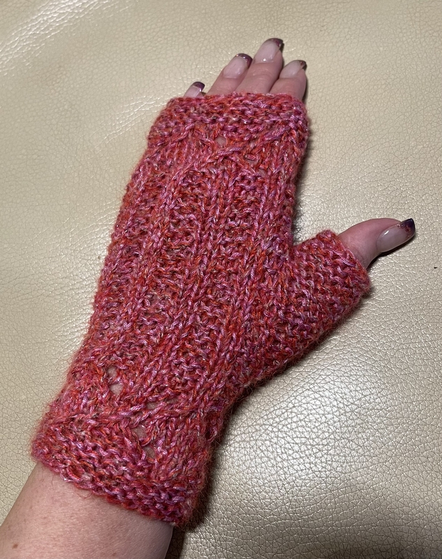 Gehäkelter, fingerloser Stulpen in Rot- und Pinktönen an einer Hand vor hellem Hintergrund.