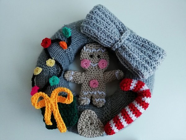Gehäkelter grauer Türkranz mit Lebkuchenmann, rot-weiß gestreifter Zuckerstange und bunter Lichterkette