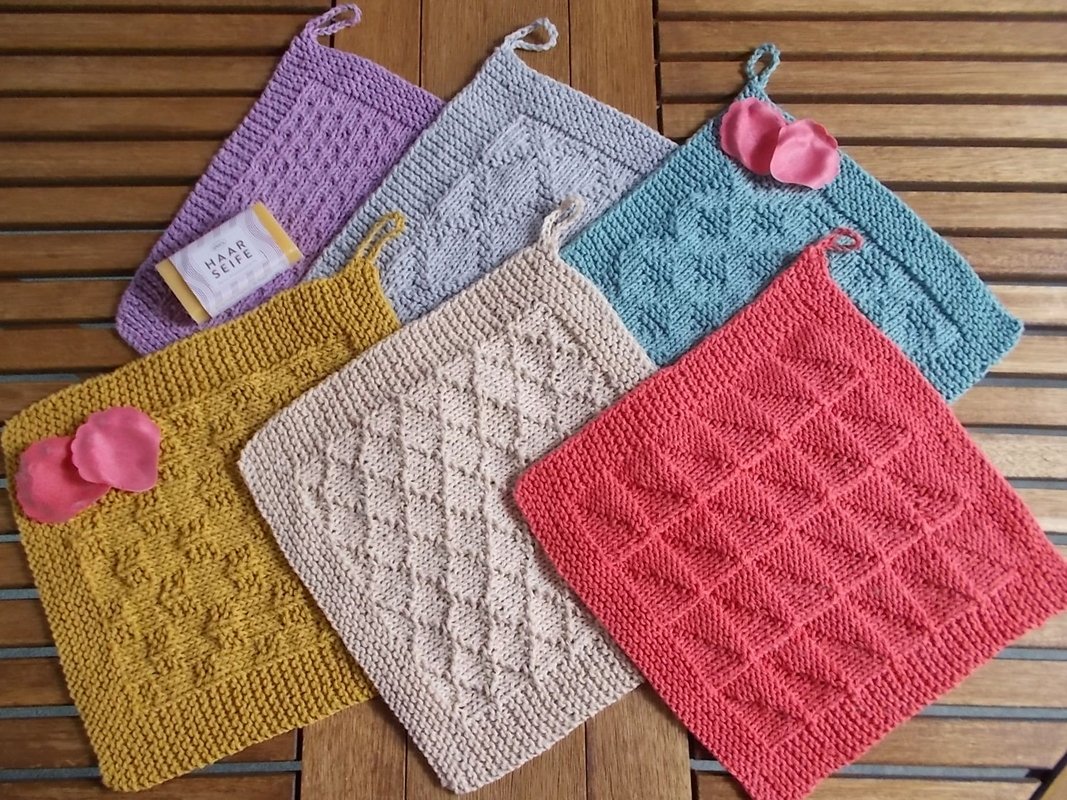 Sechs gestrickte quadratische Topflappen in Lila, Hellgrau, Türkis, Gelb, Beige und Korallrot mit Strukturmuster auf Holzlatten