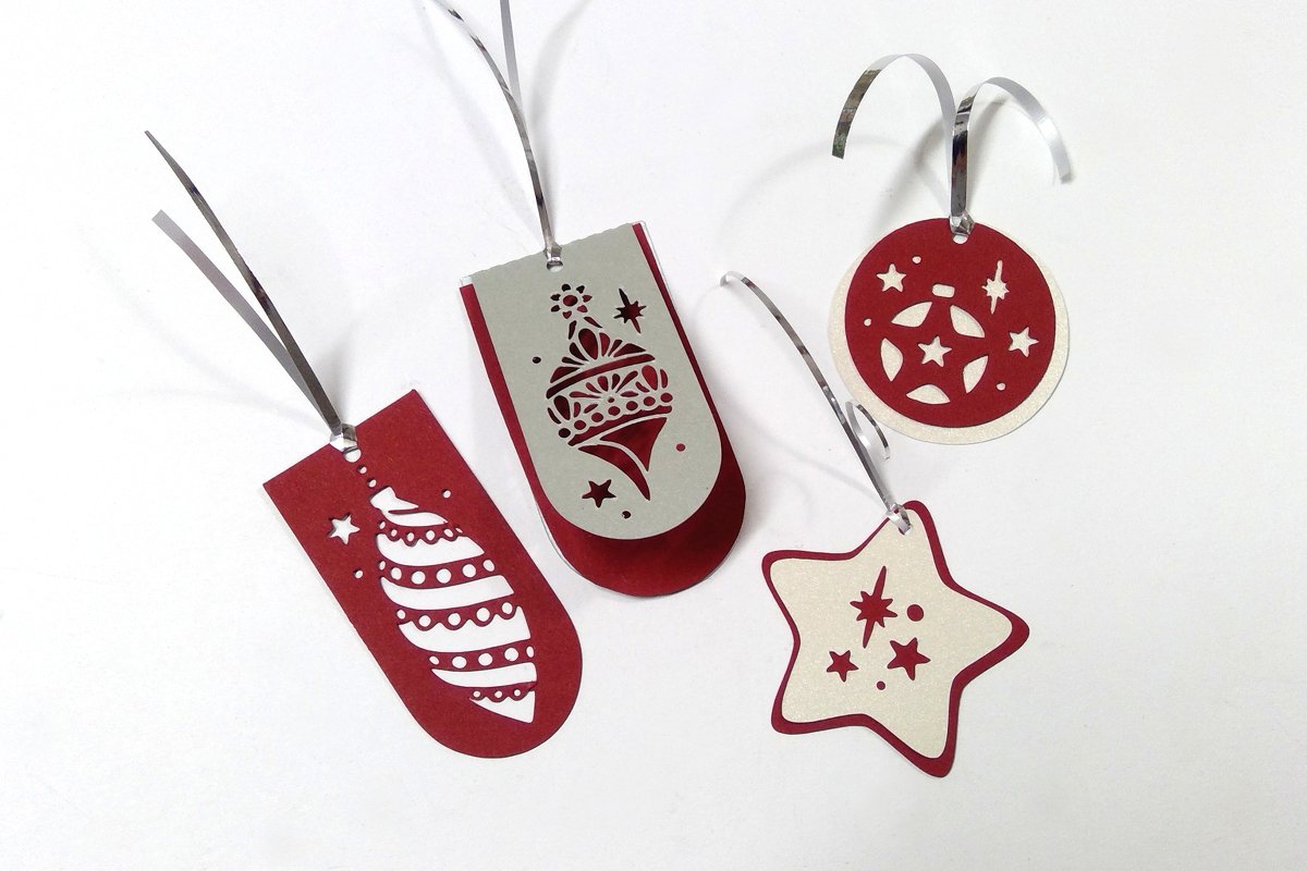 Vier unterschiedlich geformte Papieranhänger mit präzisen Ausschnitten und silbernen Aufhängebändern