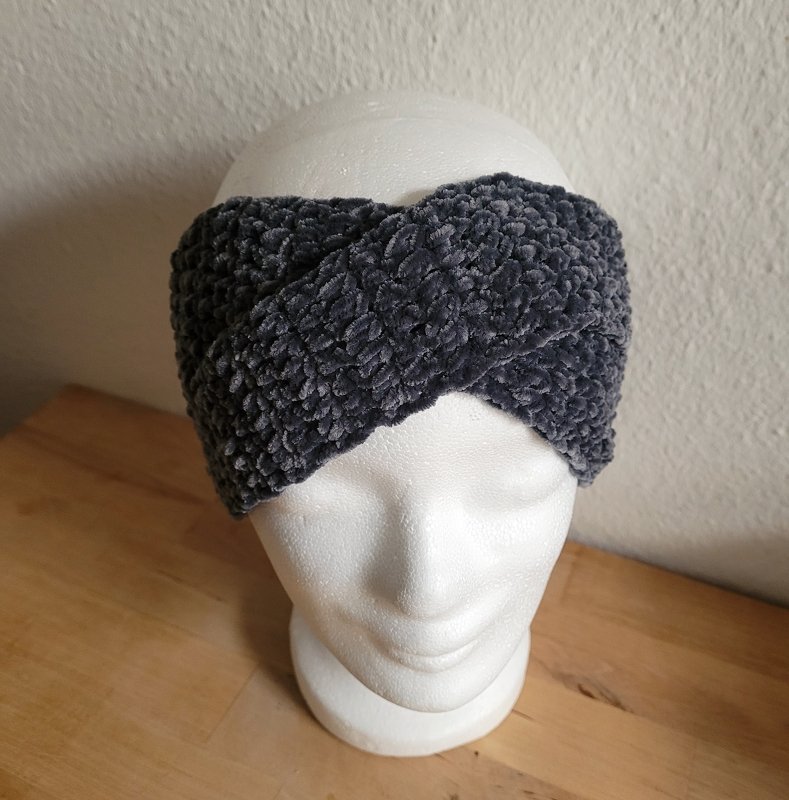 Dunkelgraues, gehäkeltes Stirnband aus flauschigem, samtartigem Garn mit gedrehter Vorderpartie auf einer Schaufenster- bzw. Styroporkopf-Büste.