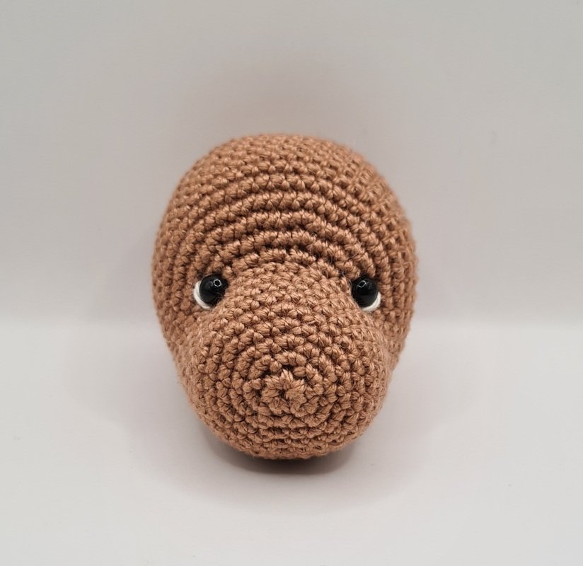 Detailaufnahme eines braunen gehäkelten Amigurumi-Kopfs mit sichtbaren Maschen und schwarzen Augen