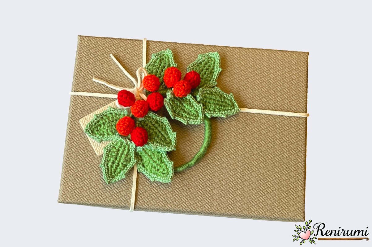 Textured brown gift box with crocheted green holly leaves and red berries tied with white string