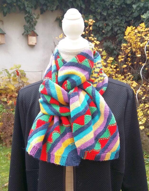 Handgestrickter, mehrfarbiger Schal mit Streifen und Dreiecksmuster an einer Schaufensterpuppe.