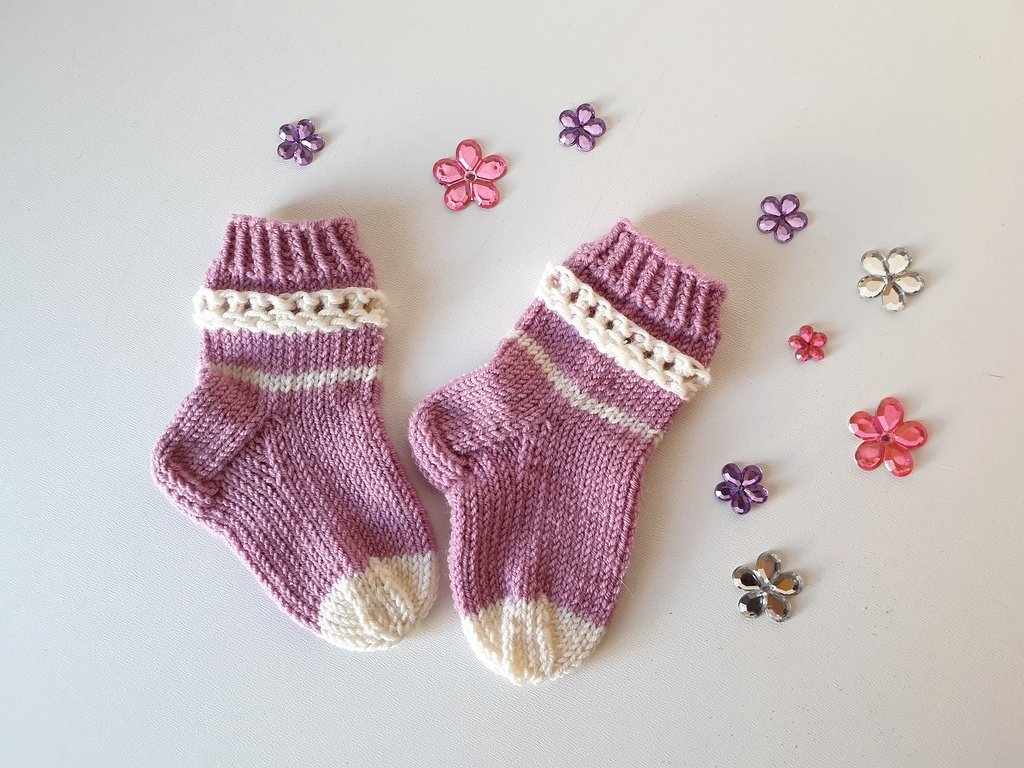 Lila-weiße handgestrickte Babysocken auf hellem Untergrund mit kleinen dekorativen Blumen