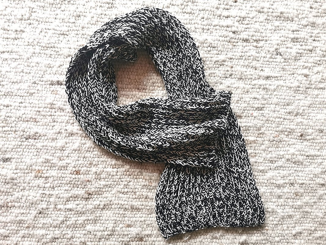 Schwarz-weißer gestrickter Schal mit Rippenstruktur auf hellem Teppich