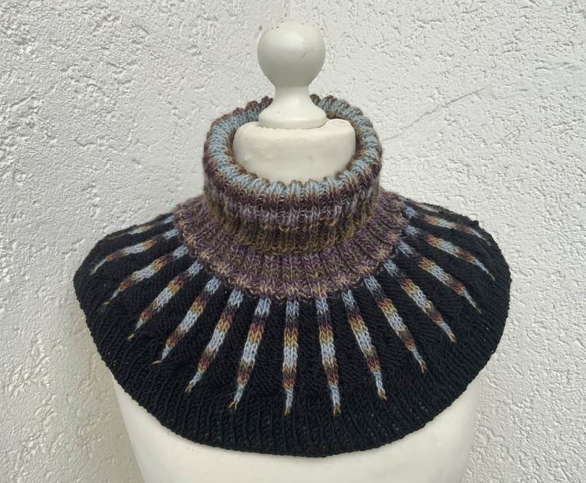 Schwarzer gestrickter Kragenschal mit hohem geripptem Rollkragen und schmalen mehrfarbigen Streifen, präsentiert an einer Schaufensterpuppe.
