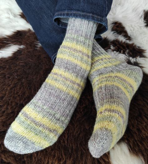Gestrickte Herrensocken in Grau und Gelb, getragen zu Jeans auf Felluntergrund
