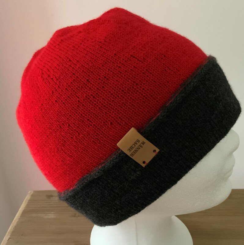 seitliche Ansicht einer rot-grauen gestrickten Mütze mit umgeschlagenem Bund und kleinem Label auf weißer Schaufensterpuppe