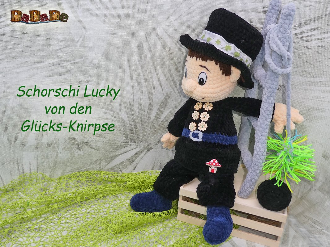 Gehäkelter Amigurumi-Schornsteinfeger mit Zylinder, Kehrbesen und Pilz-Applikation auf einer kleinen Holzkiste