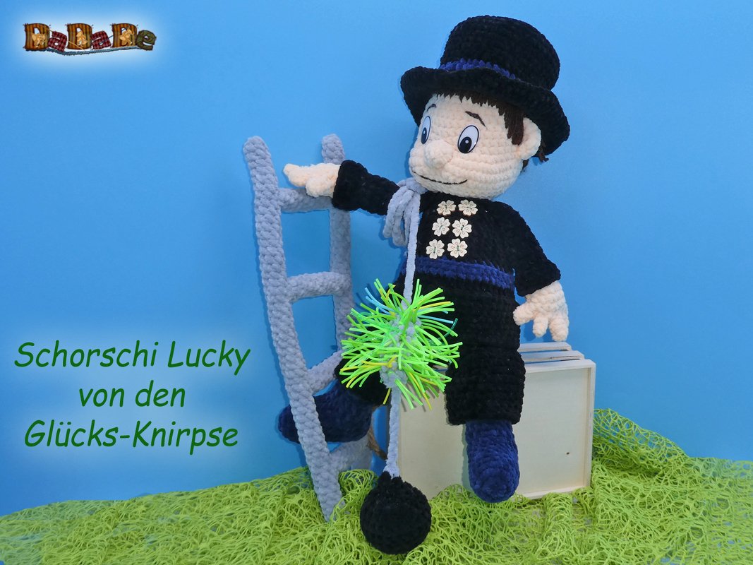Gehäkeltes Amigurumi eines Schornsteinfegers in schwarzer Kleidung mit blauem Hut, neongrüner Bürste und grauer Leiter.